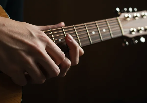 لقطة مقربة لأيدٍ تضغط على أوتار على لوحة أصابع جيتار حقيقية